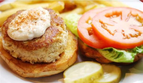 crab cake on a bun topped with sauce with lettuce and tomato on the side