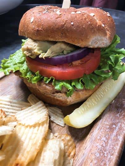chicken sandwich on a bun with lettuce, tomato and a pickle and potato chips on the side