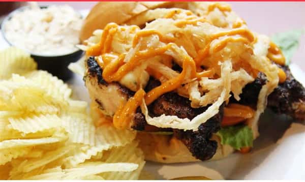grilled chicken topped with onion straws with a side of potato chips