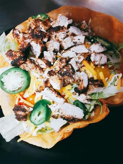 grilled chicken over lettuce with shredded cheese in a taco shell