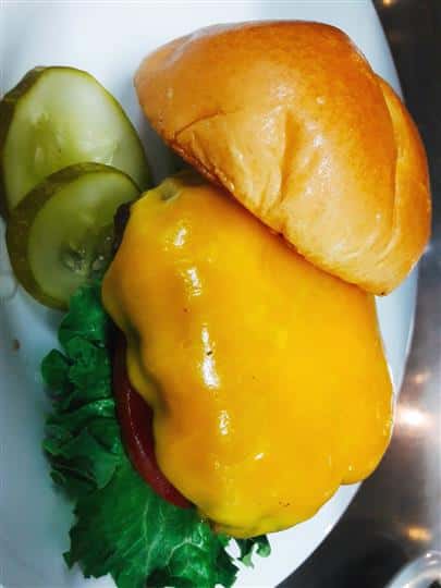 cheeseburger with lettuce and tomato on a bun with pickles on the side