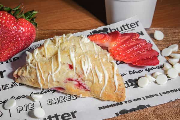 Freshly baked white chocolate strawberry scone drizzled with icing and filled with sweet strawberries at Bread and Butter Bakery.