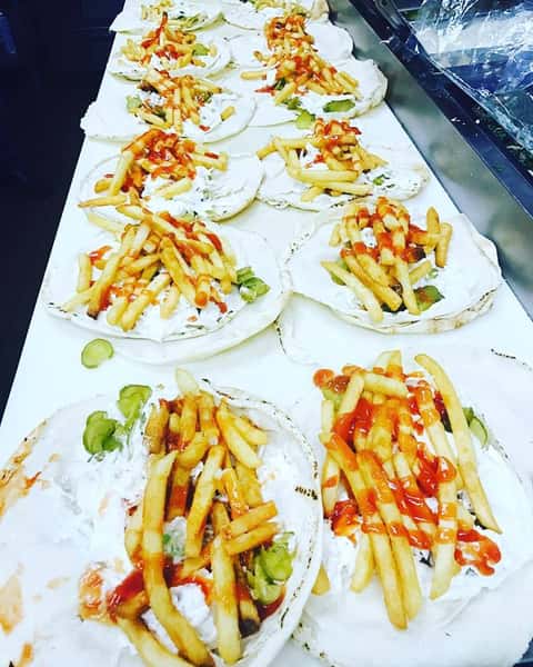assortment of tortillas topped with fries covered in yogurt and hot sauce