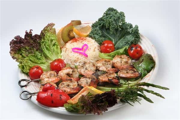 grilled shrimp skewers with a bed of rice with tomatoes and lemon wedges with pieces of lettuce