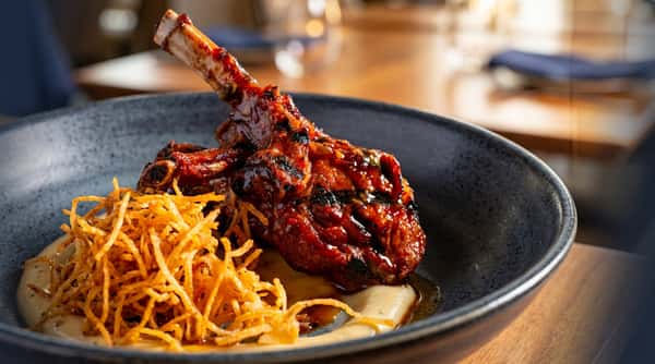 Glazed lamb chop with crispy fried onions on a bed of puree in a dark bowl.