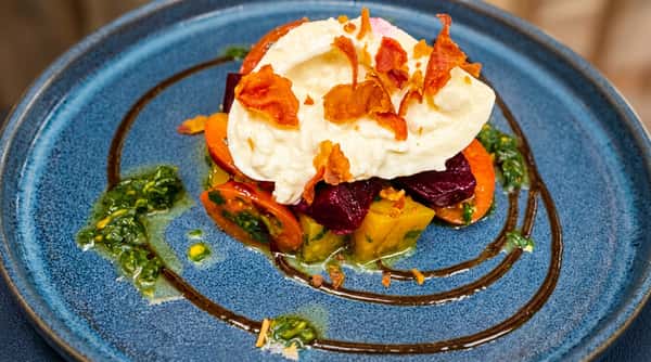 Heirloom tomato and beet salad with burrata, topped with crispy garnish, on a blue plate.