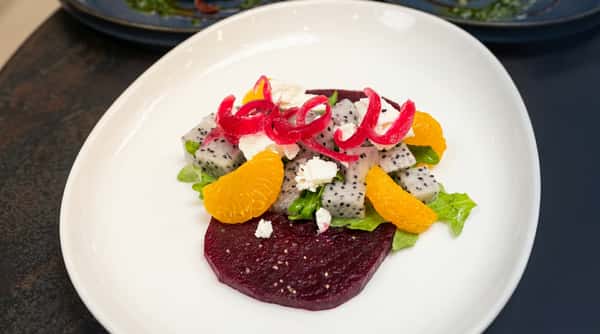 Beetroot carpaccio with dragon fruit cubes, orange segments, feta, and pickled red onion on a white plate.