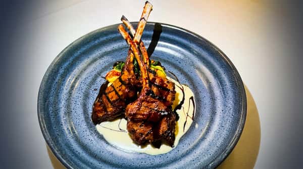 Grilled lamb chops with sauce, mashed potatoes, and greens on a blue plate.