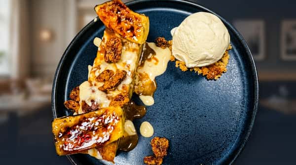 Banana bread pudding dessert with caramelized bananas, candied pecans, and vanilla ice cream on a dark plate.