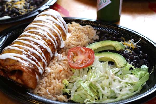 Burrito served over rice and sliced avocado with salad