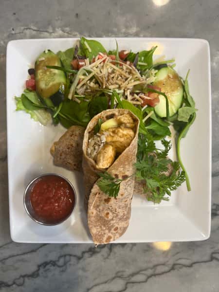Whole wheat wrap filled with bright green and orange ingredients, served with golden tortilla chips, cilantro garnish, and a side of red salsa on a white plate.