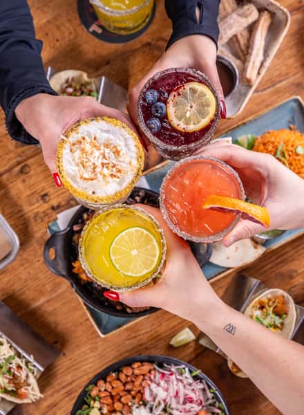 people toasting margaritas over table of food