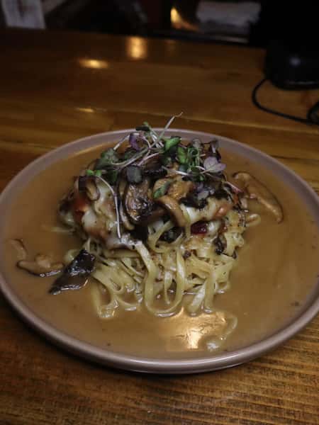 Creamy mushroom pasta with fettuccine, sautéed wild mushrooms, melted cheese, and microgreens in a cozy restaurant setting.
