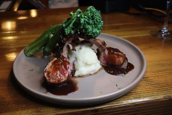 Grilled lamb chops over creamy mashed potatoes with broccolini, finished with rich red wine reduction in a warm pub setting.