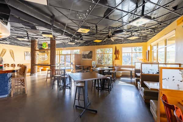 Wide-angle view of Sequoia Brewing Company's cozy taproom featuring high-top tables, wood-accented booths, large windows, and mountain lodge-style decor.