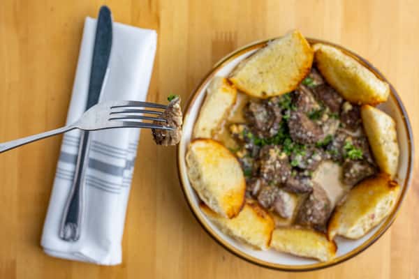 Savory beef tips smothered in brown gravy and topped with herbs, surrounded by toasted garlic bread wedges in a hearty bowl.