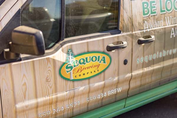 Side profile of a Sequoia Brewing Company van featuring rustic wood-panel branding, green trim, contact details, and promotional messaging about local award-winning ales.