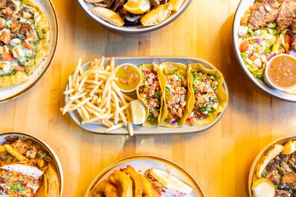 Overhead view of vibrant chicken street tacos topped with fresh pico de gallo and cotija cheese, served with French fries and salsa, surrounded by assorted entrees