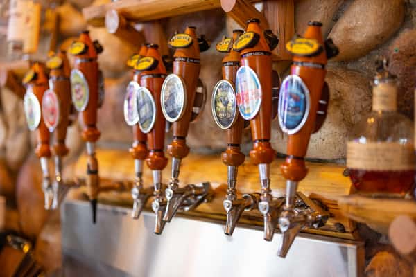 Angled close-up of Sequoia Brewing's wooden craft beer tap handles mounted on a stone wall, each labeled with unique house brews.