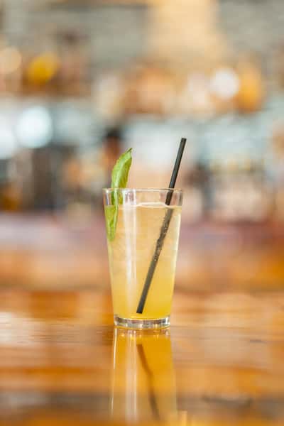 Refreshing citrus cocktail served in a tall glass over ice, garnished with a fresh basil leaf and black straw, set on a glossy wooden bar at Sequoia Brewing Company.