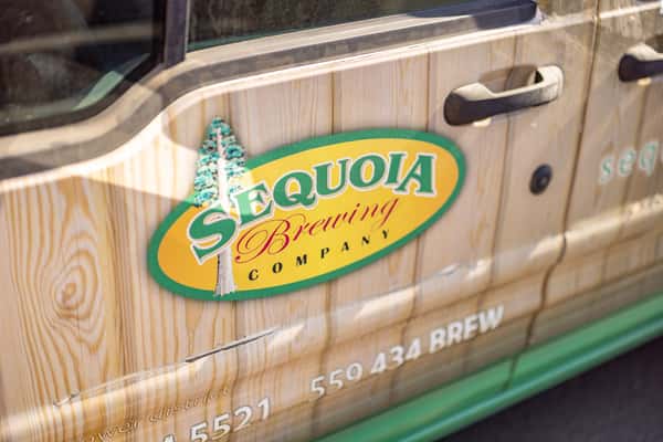 Side view of a Sequoia Brewing Company delivery van featuring rustic wood grain graphics and branded logo decal with bold green and yellow typography.