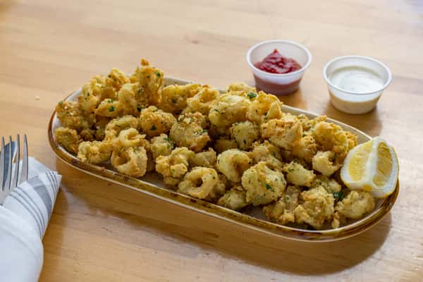 Crispy fried calamari rings seasoned with herbs, served with lemon wedges, marinara sauce, and creamy ranch dip on a long appetizer plate.