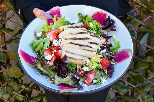 Colorful grilled chicken salad with mixed greens, fresh strawberries, watermelon radish slices, crumbled feta, and candied pecans, served in a wide white bowl.