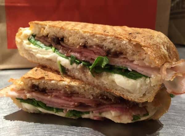 A toasted panini with ham, cheese, and spinach
