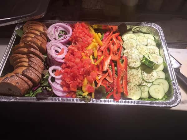 Catering tray filled with lettuce, tomato, peppers, cucumbers, and a side of sliced bread