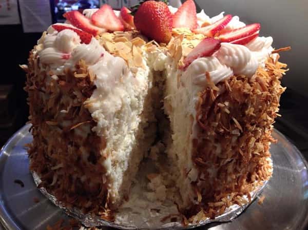 Cake with coconut outside and topped with icing, sliced almonds, and strawberries. Vanilla cake on the inside