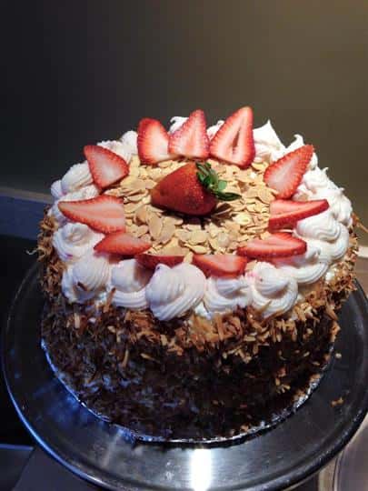 Cake with coconut coated outside, topped with icing, sliced almonds, and strawberries