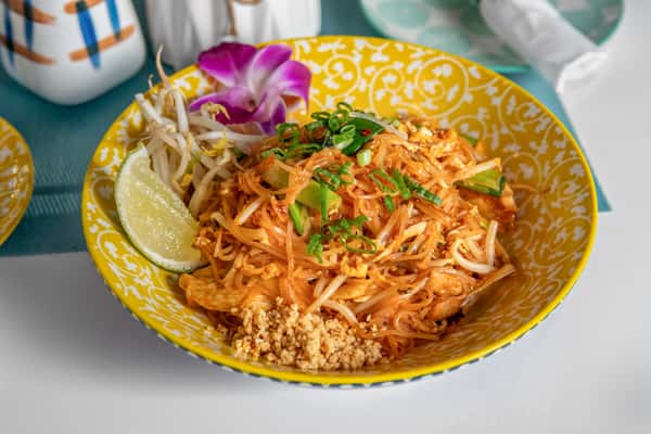 bowl of chicken pad tha with a lime wedge and flower garnish