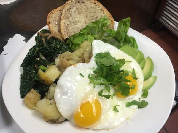 Eggs over avocado, potatoes, lettuce, spinach, and bread