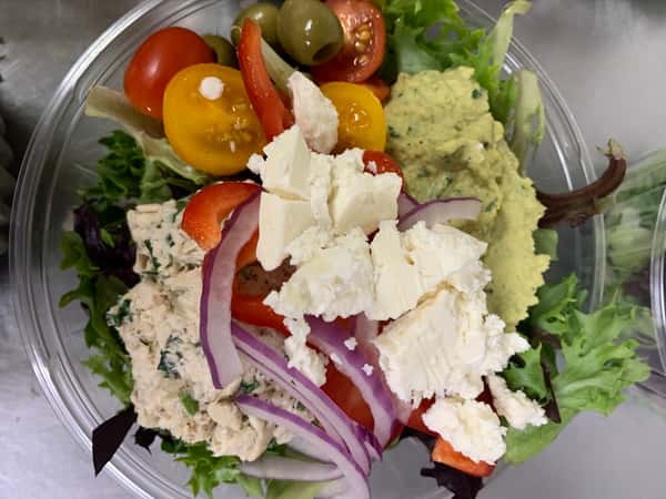 A salad with mesclun greens, topped with feta cheese, tomato, onion, olives, and an avocado spread.