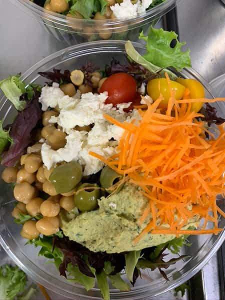 A salad with mesclun greens, topped with shredded carrots, tomatoes, chickpeas, olives, and avocado spread