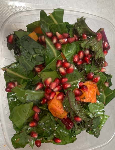 A spinach salad with pomegranates and sweet potatoes in a to-go container