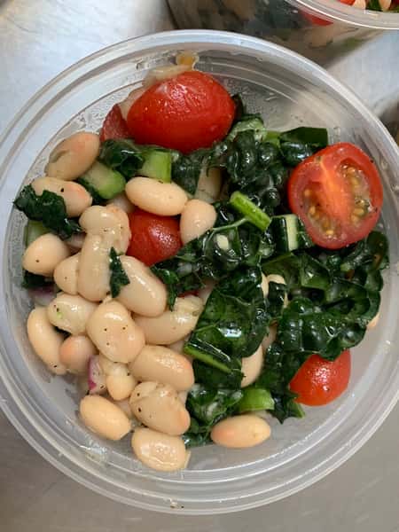 Cannellini beans with leafy greens and cherry tomatoes, topped with a light dressing in a to-go cup