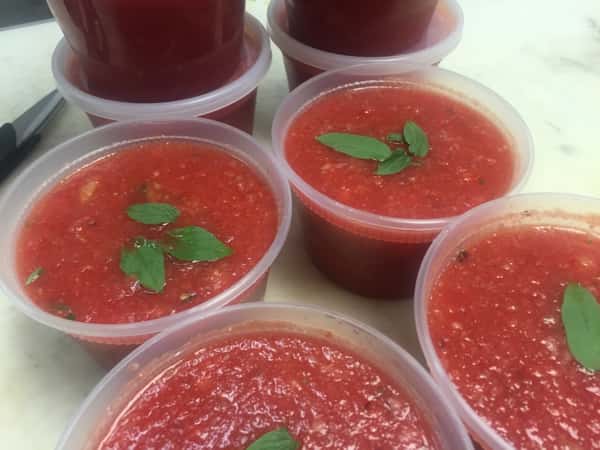 Containers filled with fresh tomato sauce and garnished with fresh basil leaves