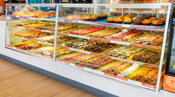 Glass display case filled with rows of various donuts, pastries, and muffins like Red Velvet, Caramel Cake, and Oreo Chocolate.
