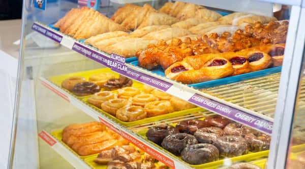 Display case filled with rows of pastries, including apple turnovers, bear claws, cherry cream cheese danishes, and glazed donuts.