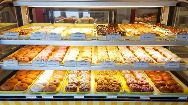 Display cases filled with rows of various donuts, pastries, muffins, and danishes in a bakery or cafe.