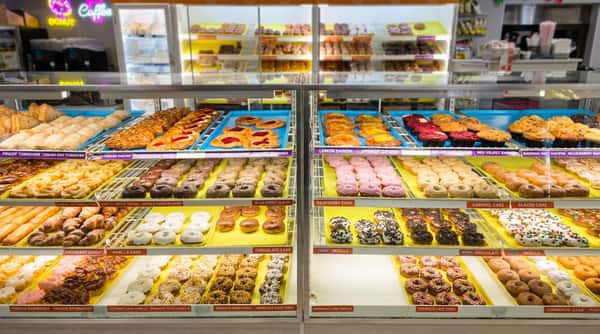 Display cases filled with rows of various donuts, pastries, muffins, and danishes in a bakery or cafe.