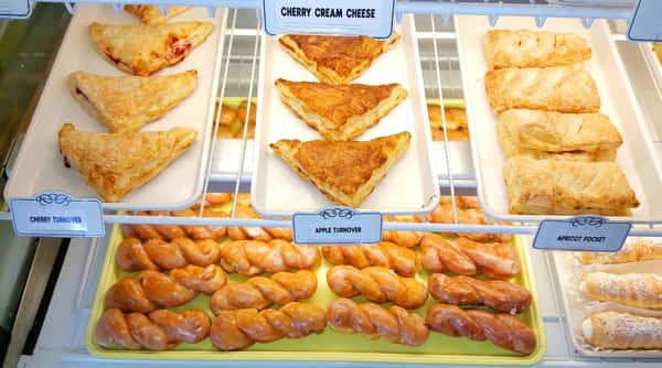 Bakery display case with cherry turnovers, apple turnovers, apricot pockets, and glazed twisted donuts.