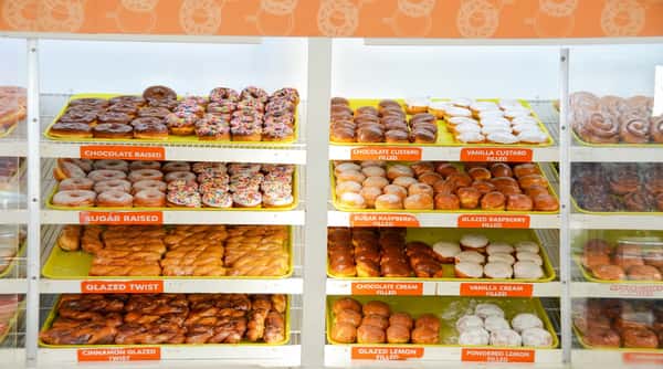 Doughnut display case with trays of chocolate raised, sugar raised, twists, and filled doughnuts.