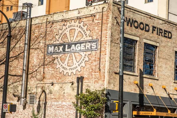 Brick exterior of Max Lager's American Grill & Brewery featuring vintage-style signage reading "Wood Fired, Fresh Brewed" with an industrial-meets-historic charm. Ideal for SEO keywords: Atlanta brewery, wood-fired restaurant, craft beer dining.