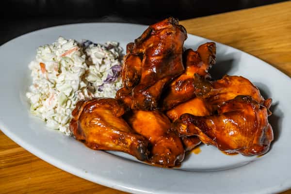 Glossy barbecue wings served with a side of coleslaw on a white plate. A tangy, smoky appetizer perfect for game day or casual dining.