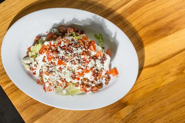 Top-down view of a classic wedge salad with iceberg lettuce, blue cheese dressing, bacon crumbles, and diced tomatoes. A crisp and creamy appetizer perfect for steakhouse menus.
