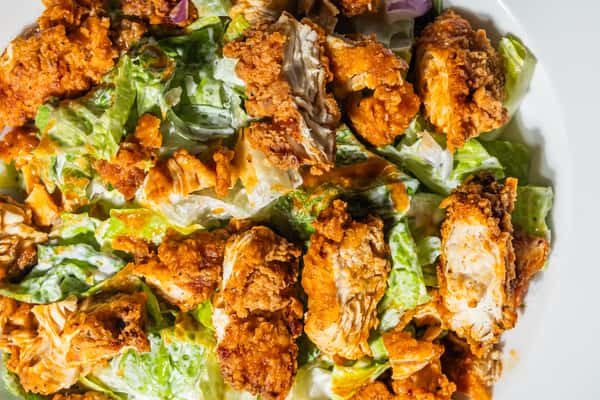 Chopped romaine lettuce tossed in ranch dressing and topped with crispy buffalo chicken strips, drizzled with hot sauce. A hearty, flavorful salad blending spicy, creamy, and crunchy textures in every bite.