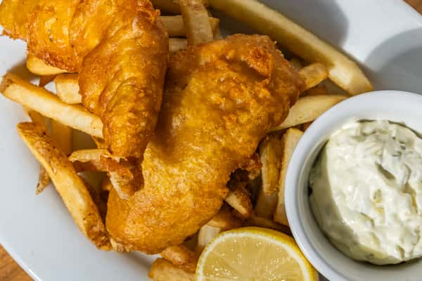 Crispy beer-battered fish fillets served over golden fries with tartar sauce and a lemon wedge. A classic British pub dish with an American twist, ideal for seafood lovers.
