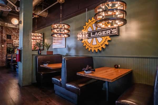 Cozy booth seating area at Max Lager's featuring dark leather upholstery, wooden tables, and illuminated hanging lights with Max Lager's logo on the wall. A welcoming, stylish interior perfect for casual dining.